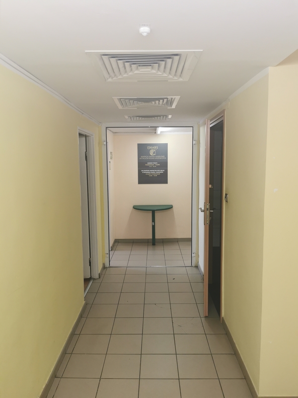 Zdjęcie przedstawia korytarz prowadzący do sekretariatu Inspektoratu z wind. Na ścianie widzimy zieloną tablicę informacyjną Inspektoratu. 